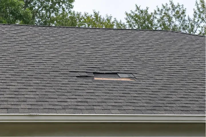 Asphalt shingle roof with damaged and missing shingle patches.